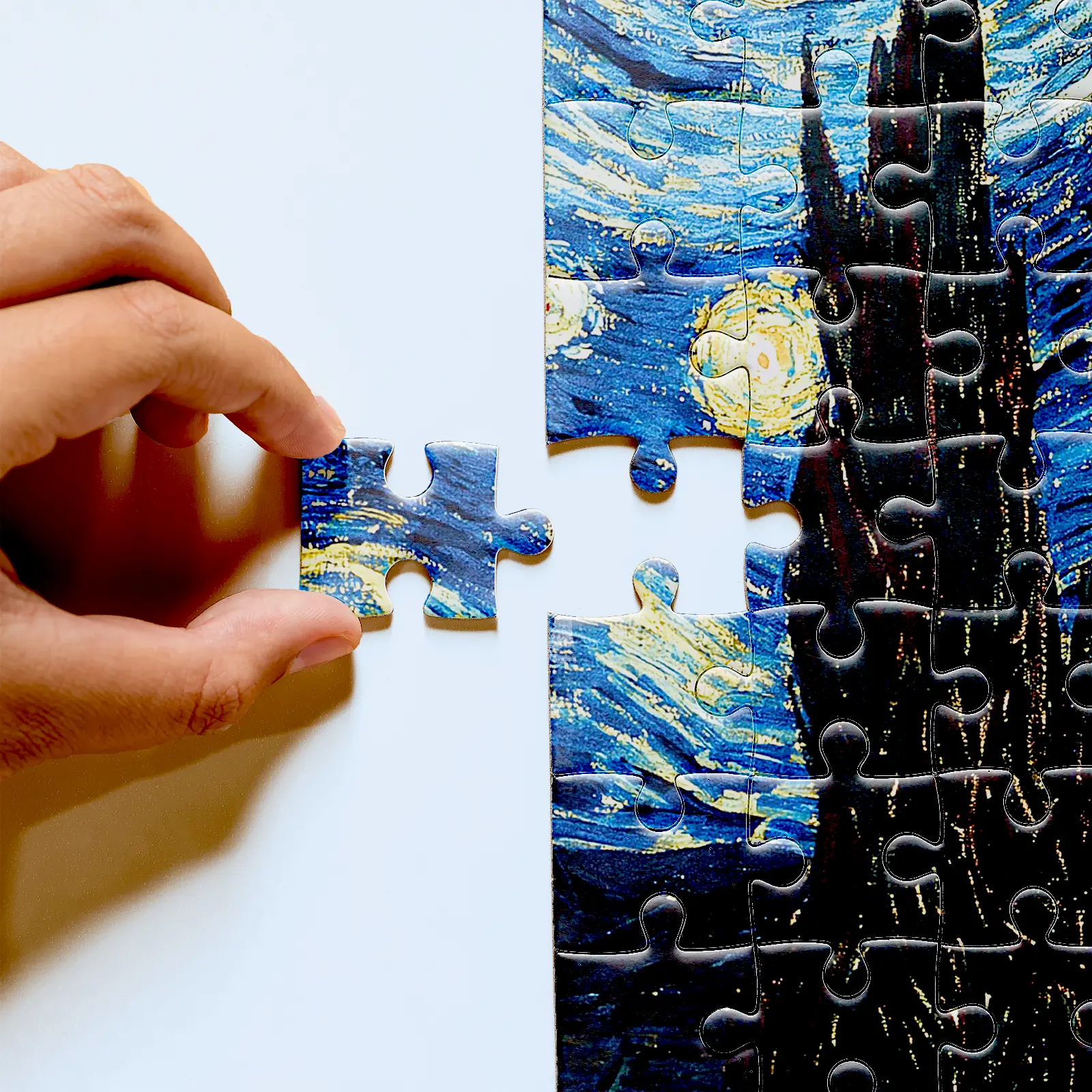 Hand holding a Starry Night puzzle piece beside the blue sky and dark cypress
