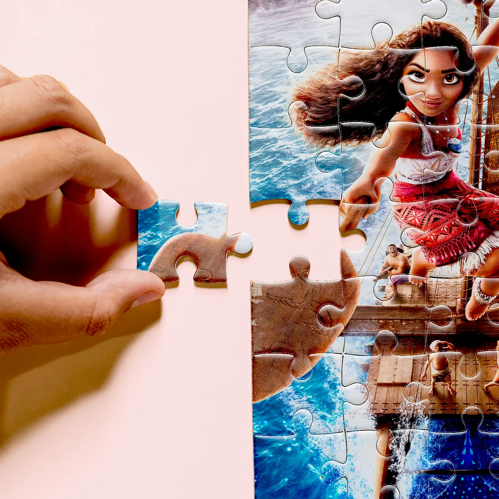 Hand holding a puzzle piece beside the Moana artwork