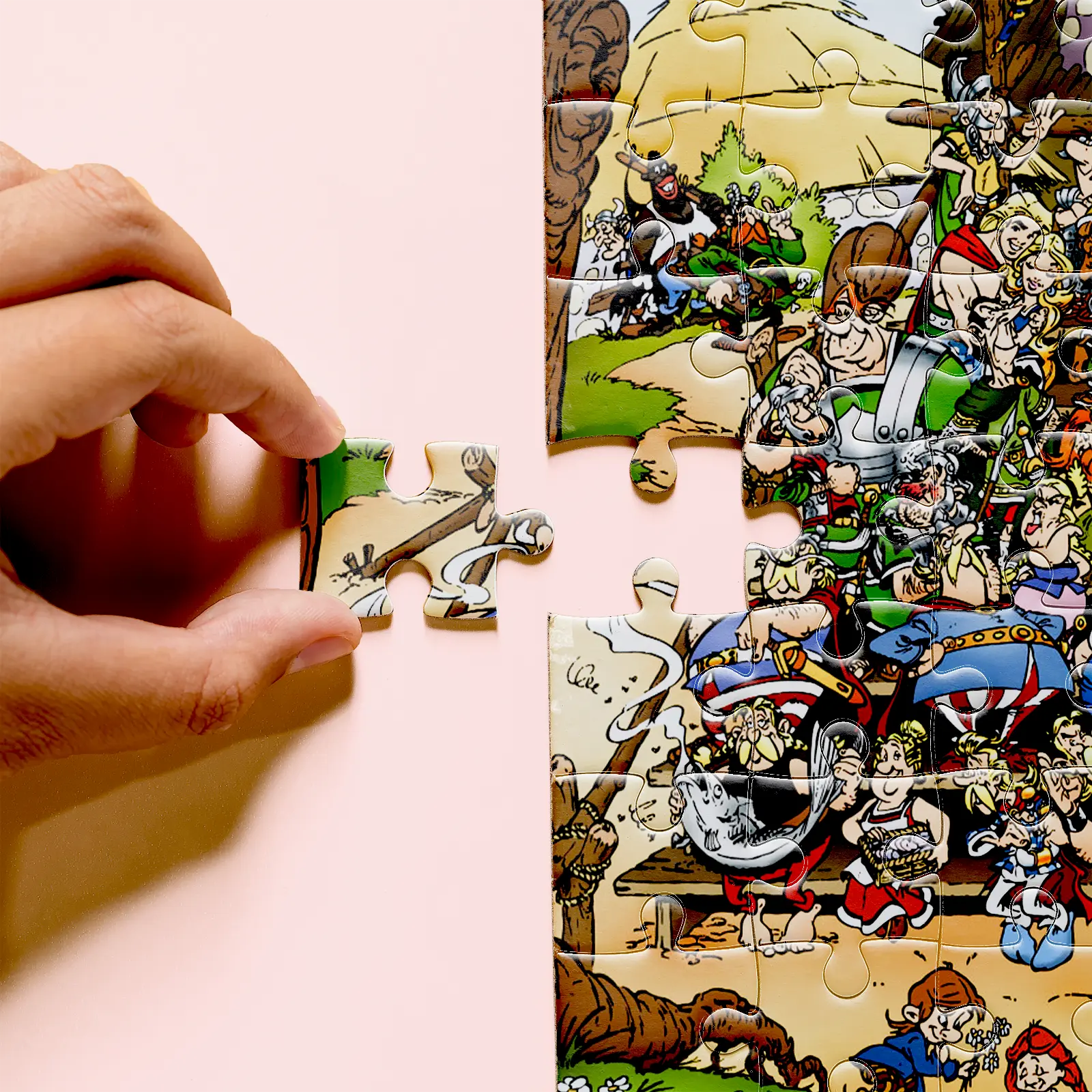 Hand holding an Asterix puzzle piece beside the partially assembled puzzle